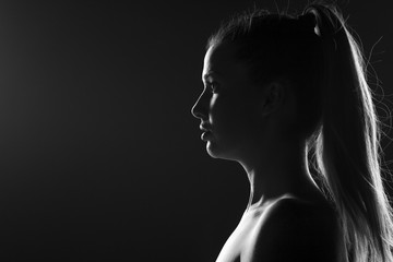 silhouette profile of a young woman with a ponytail on a dark background - obrazy, fototapety, plakaty