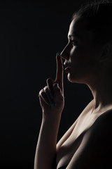 silhouette of a woman with a finger in front of lips on a dark background