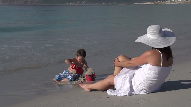 Young boy playing on the beach while mother looks on, Cape Town,South Africa