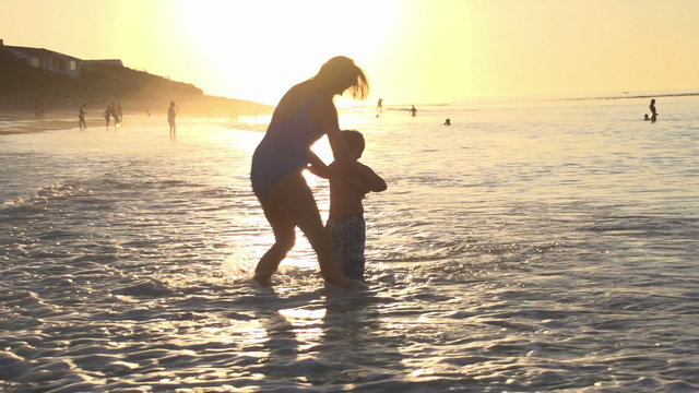 Mother and young boy playing in shallow water on beach in silhouette at sunset, Cape Town,South Africa