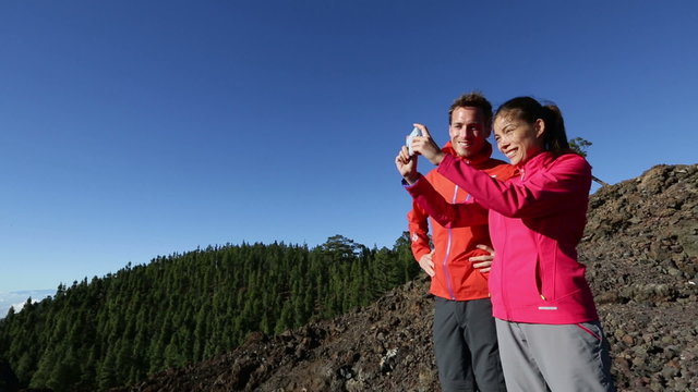 Hiking couple using smartphone camera taking pictures outdoors on hike. Happy people taking photos with smart phone in beautiful mountain nature landscape.