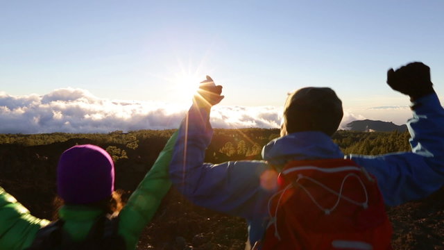 Freedom - Happy couple cheering and celebrating running. Hiking man and woman raising arms excited in celebration outdoors. Hikers at sunset in mountain enjoying mountain top summit and success.