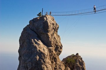 People crossing the chasm on the hanging bridge. Black sea background, Crimea, Russia