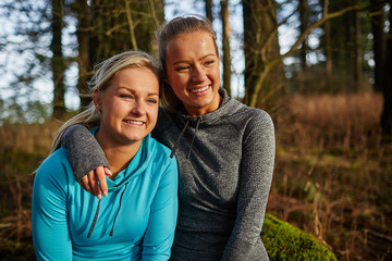 two beautiful young girls sitting on log arms around watching su
