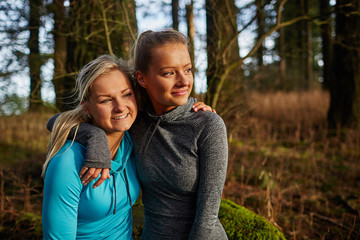 Naklejka premium two beautiful young girls sitting on log arms around watching su