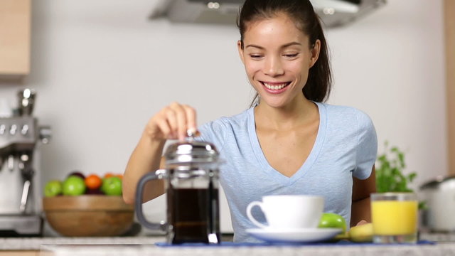 Woman making french press coffee at breakfast. Happy smiling girl drinking coffee eating breakfast at home in kitchen. Mixed race Asian Caucasian female model.