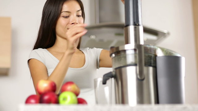 Woman making apple and vegetable juice on juicer machine at home in kitchen. Juicing and healthy eating happy woman making green vegetable and fruit juice. Mixed race Asian Caucasian model.