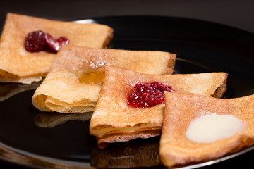Pancakes with strawberry jam, raspberry jam , sour cream and honey on a black plate