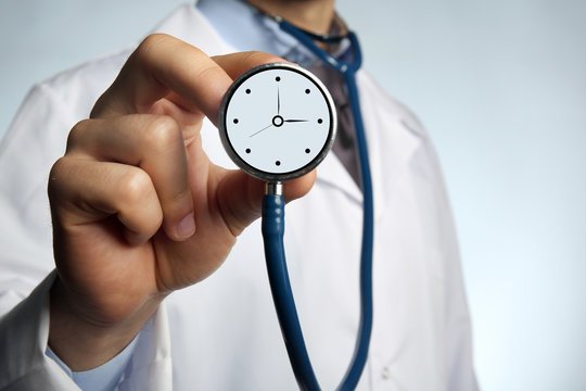 Male doctor holding stethoscope with clock