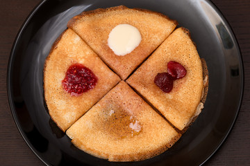 Pancakes with strawberry jam, raspberry jam , sour cream and honey on a black plate