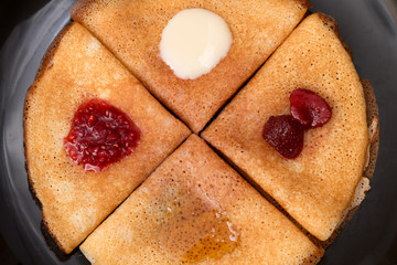 Pancakes with strawberry jam, raspberry jam , sour cream and honey on a black plate