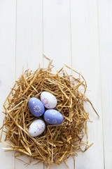 Colorful Easter Eggs in the nest of straw on the white wooden background