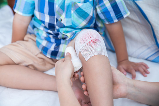 Child injured. Mother bandaging son's knee.