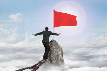 Man balancing on rusty chain for flag on mountain top