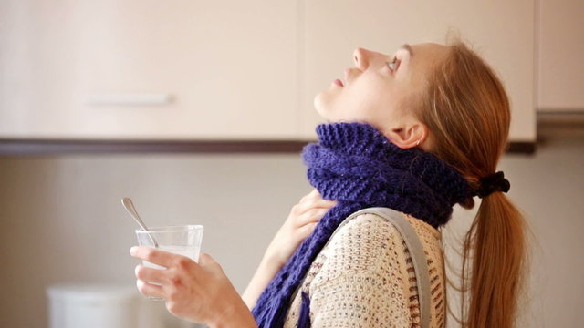 Girl with quinsy taking medicine and gargling throat in kitchen