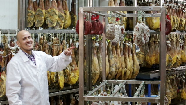 Worker in white gown checking drying sausages in workshop