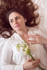 Beautiful young woman with beautiful long hair, lying on the bed holding a freesia flower