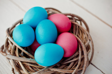 blue and pink Easter eggs in nest on white wooden background
