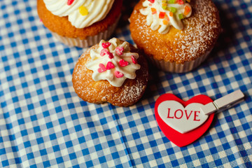 Beautiful cupcakes and a heart with the inscription Love lie on a vintage checkered tablecloth