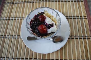 Berries (strawberries, blueberries, blackberries) dessert with yogurt and rice flakes in glass cup. Finished dish.