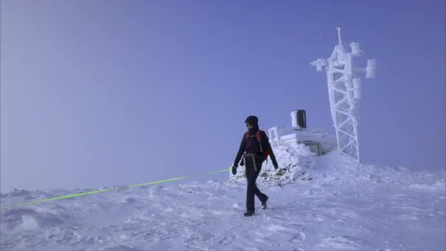 A hiker and their dog leaving a frozen weather station on the summit of Cairn Gorm in the Scottish Highlands on a cold sunny winters day.