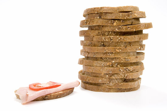 Stack Slices Of Granary Bread And Sandwich With Ham And Tomato On White Background