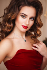 Beautiful young woman with perfect make up and hair style in gorgeous red evening dress in expensive luxury interior