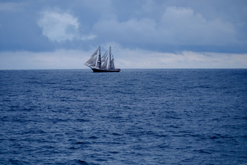 Fototapeta na wymiar Segelschiff, Zweimaster, leuchtend weiß, auf weiter blauer, klarer Wasserfläche mit Wolken