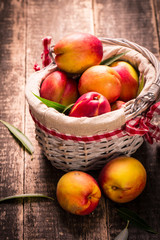 Fresh peaches in a basket on rustic wooden table.