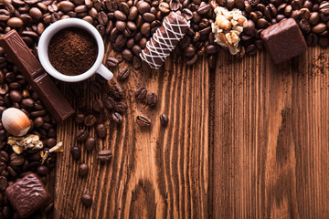 Gebrande koffiebonen, chocolade, snoep, noten, beker en de plek voor inscripties op houten achtergrond