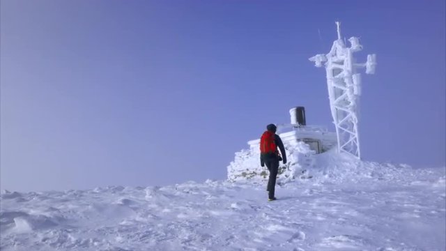 A hiker approaching a frozen weather station on the summit of Cairn Gorm in the Scottish Highlands on a cold sunny winters day.