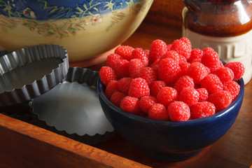 Raspberries in a blue bowl , metal baking tarts, milk bottle and