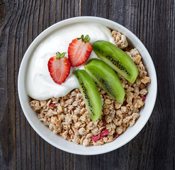 Healthy breakfast, bowl of granola with yogurt and fresh fruits on wooden table, top view