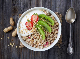 Healthy breakfast, bowl of granola with yogurt and fresh fruits on wooden table, top view