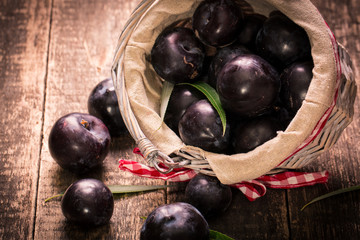 Fresh plums in a basket on rustic wooden table.