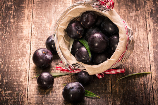 Fresh plums in a basket on rustic wooden table.