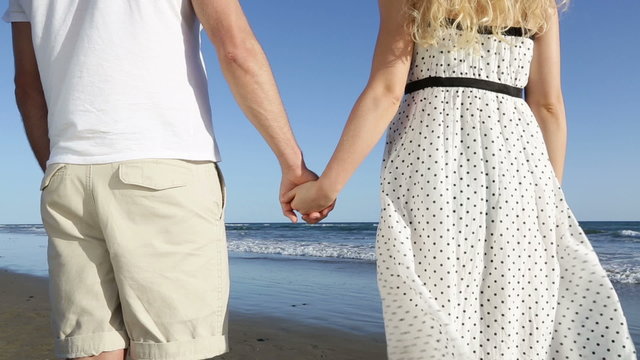 Couple holding hands - romantic lovers on beach. Close up of young lovers holding hands from behind enjoying view of ocean sea during holidays vacation travel.