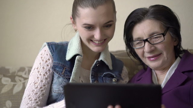 Girl and old woman using a tablet at the sofa, smiling, caring