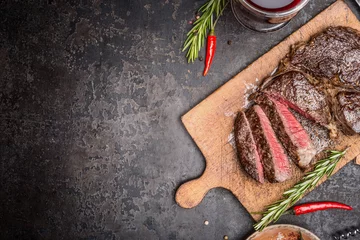  Sliced medium rare grilled steak on rustic cutting board with rosemary and spices , dark rustic metal background, top view, place for text © VICUSCHKA