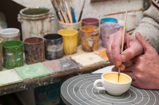 A pottery decorator finishing a ceramic small cup with floral motifs in his work table in Caltagirone, Sicily