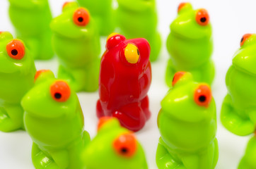 Small plastic toy frogs. One red and the other green. Close up view. Frogs are dense structure. Different from the others. At home among strangers.