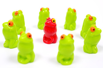 Small plastic toy frogs. One red and the other green. Close up view. Frogs are dense structure. Different from the others. At home among strangers.