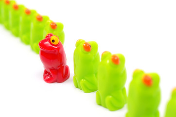 Line of green toy frogs. Among them, one red frog. Close up view. Different from the others. At home among strangers. Concept of antagonism.