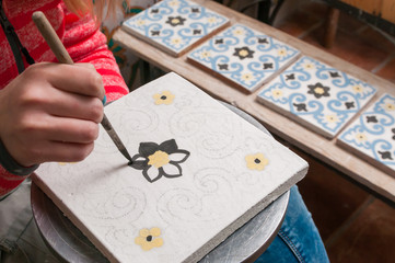 Naklejka na ściany i meble A pottery decorator painting a ceramic tile with floral motifs in his work table in Caltagirone, Sicily