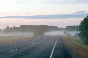 Rural road with headlights of car appearing through the fog