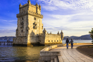 Belem Tower Lisbon Portugal at sunset with romantic couple walking near the river Tejo historic fortress and UNESCO world heritage site Torre de Belem high resolution wall art travel decor © Freesurf