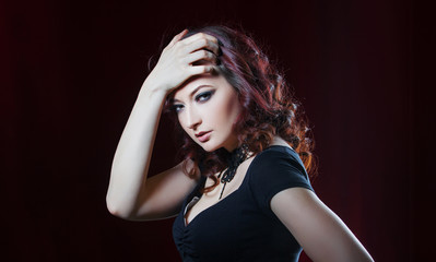 beautiful brunette in  black dress on a background of red curtain