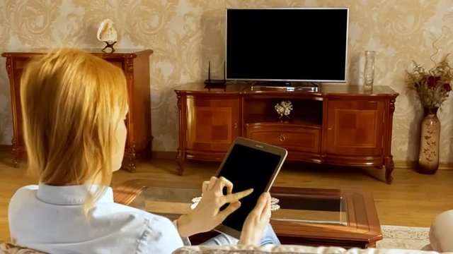 Young woman using tablet and watching television in living room. Shoot behind model's shoulders. Alpha Channel included.