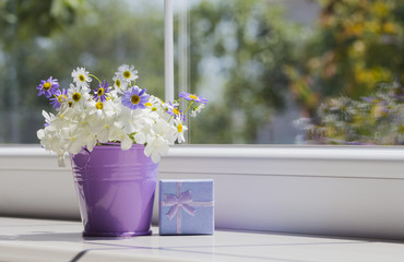 Small purple bucket with daisies and blue gift box near the wind