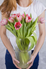 Bouquet of pink tulips in large glass vase in hands of beautiful